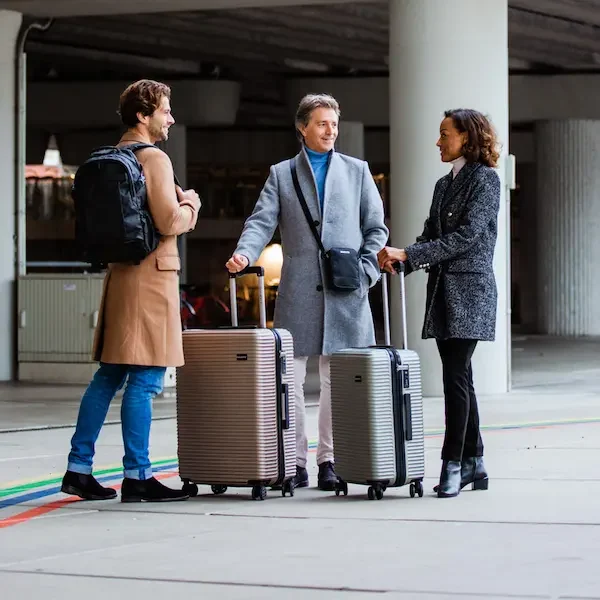 Reisekoffer in Verschiedenen Farben, Größen bei Koffer.live Drei Reisende stehen mit Koffern in einem Parkhaus, umgeben von bunten Linien.
